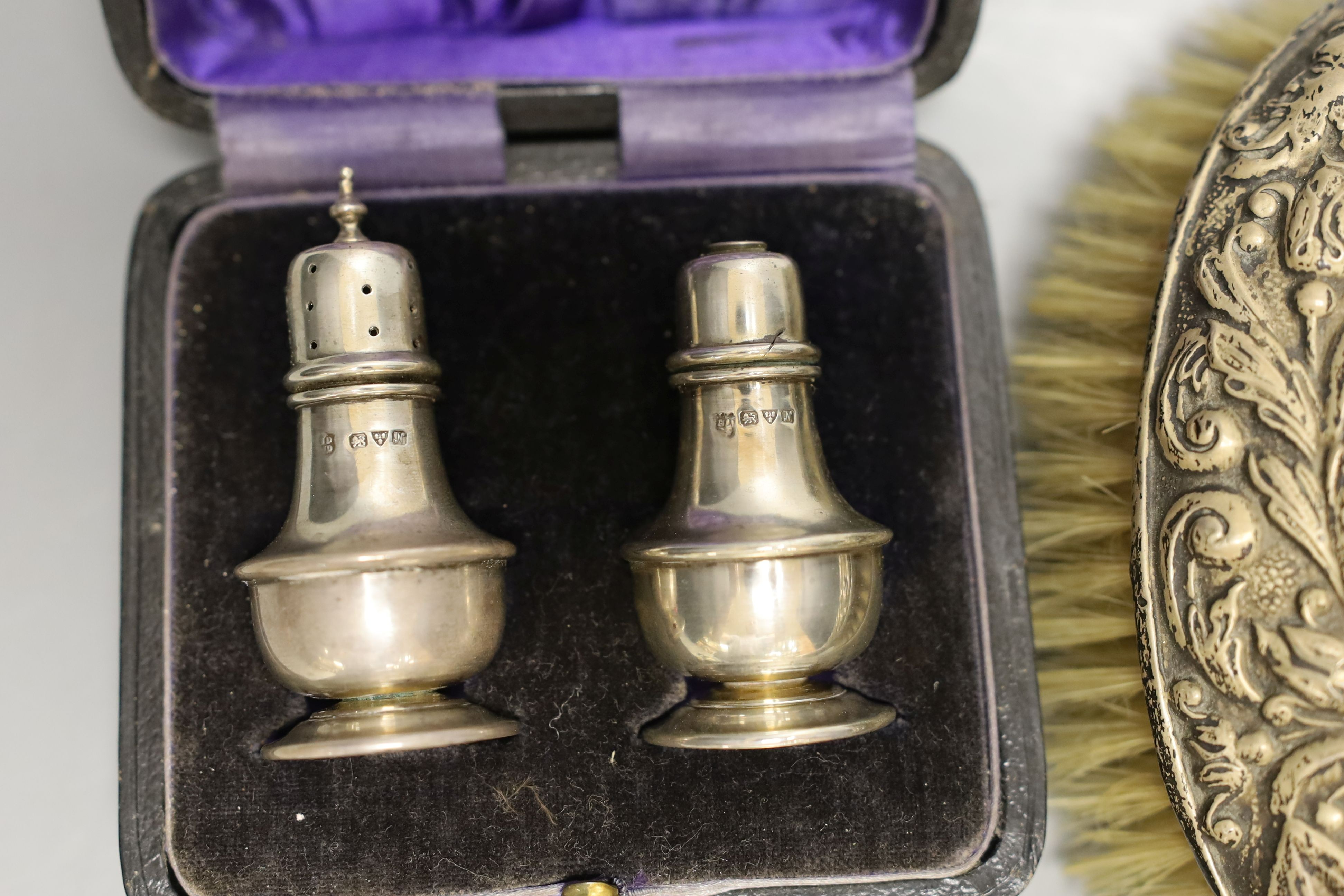 A cased pair of George V silver condiments, an engraved silver purse, silver mounted mirror and brush an a child's silver rattle.